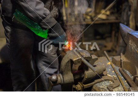 Blacksmith quenching hot iron part 98549145