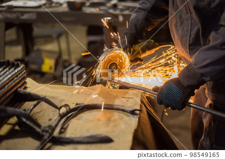 Blacksmith sawing metal with hand circular saw 98549165