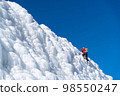 A climber in a red suit climbs an icy white mountain 98550247