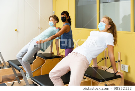 Teenagers in masks training pilates in gym with traine Teenagers in masks training pilates in gym with traine 98552132