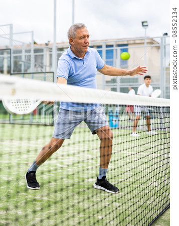 Sporty senior man playing padel on open tennis court 98552134