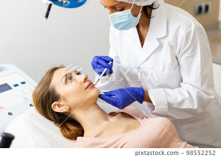 Cosmetologist making injections of botulotoxin into lips of young woman 98552252
