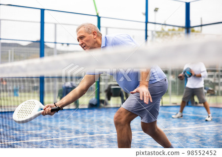 Aged man playing paddleball match on outdoor court Aged man playing paddleball match on outdoor court 98552452