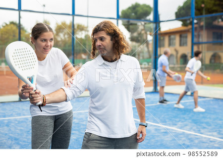 Girl teaching man to play padel tennis on outdoor court Girl teaching man to play padel tennis on outdoor court 98552589