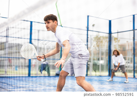 Focused teenager playing paddleball match on outdoor court 98552591