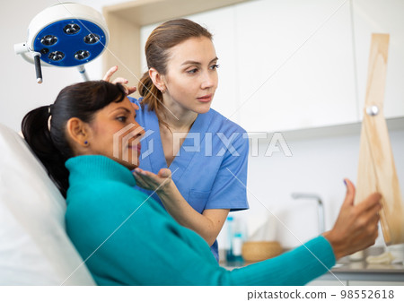 Beautician examining face skin of female patient Beautician examining face skin of female patient 98552618