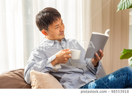 男人在客廳裡一隻手拿著咖啡看書 男人在客廳裡一隻手拿著咖啡看書 98553918