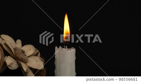 Burning wax candle and flowers against a black background 98556681