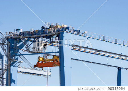 Large lifting structures with suspended spreader for cargo containers on the background of the blue sky Large lifting structures with suspended spreader for cargo containers on the background of the blue sky 98557064