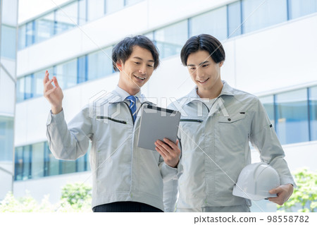 A young worker looking at a tablet in front of a building and a foreman.Photography cooperation "LINK FOREST" A young worker looking at a tablet in front of a building and a foreman.Photography cooperation "LINK FOREST" 98558782