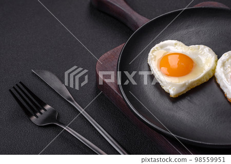 Two heart-shaped fried eggs on a black ceramic plate on a dark concrete background Two heart-shaped fried eggs on a black ceramic plate on a dark concrete background 98559951