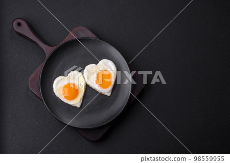 Two heart-shaped fried eggs on a black ceramic plate on a dark concrete background Two heart-shaped fried eggs on a black ceramic plate on a dark concrete background 98559955