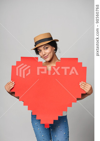 Mixed race girl in straw hat holding big paper pixel style heart shape with copy space for text Mixed race girl in straw hat holding big paper pixel style heart shape with copy space for text 98560768