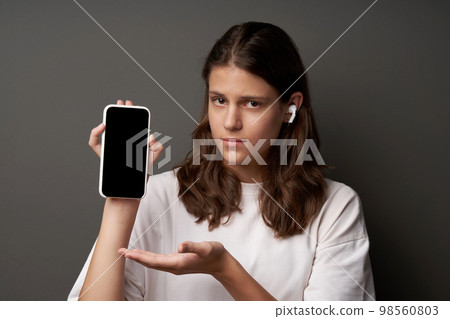 Sad young woman showing presenting blank mobile phone screen Sad young woman showing presenting blank mobile phone screen 98560803