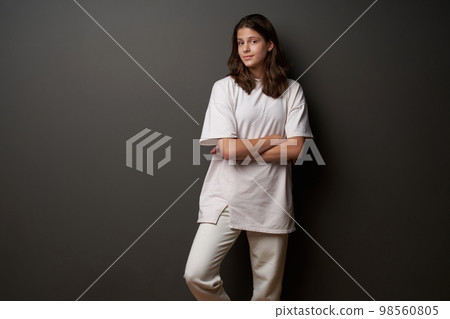 Confident casual girl wearing loose fit clothes standing with folded hands on dark background Confident casual girl wearing loose fit clothes standing with folded hands on dark background 98560805
