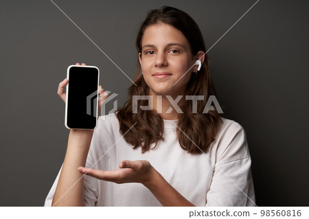 Casual natural calm woman pointing finger at blank mobile phone screen isolated over gray background Casual natural calm woman pointing finger at blank mobile phone screen isolated over gray background 98560816