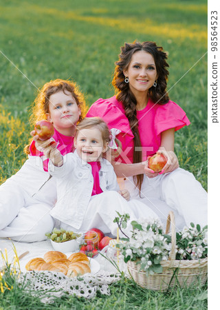 Cute mom and two daughters are having a picnic in the spring garden. Outdoor activity. Sweet moments family 98564523