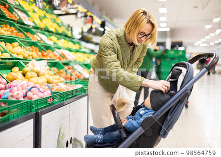 Casualy dressed mother buying fruits and vegetables in supermarket grocery store with her infant baby boy child in stroller Casualy dressed mother buying fruits and vegetables in supermarket grocery store with her infant baby boy child in stroller 98564759