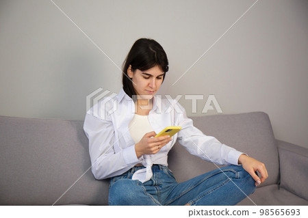 A woman in a white shirt with a smartphone in her hands A woman in a white shirt with a smartphone in her hands 98565693