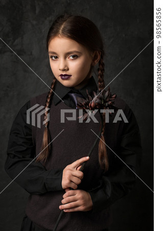 A sullen little girl with pigtails is holding a black dahlia flower A sullen little girl with pigtails is holding a black dahlia flower 98565856