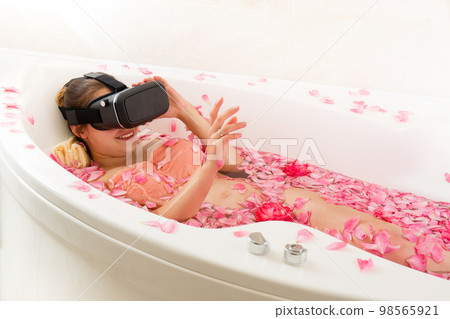 A pregnant woman in 3D virtual reality glasses rests in a bath with rose 98565921