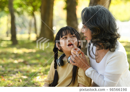 Smiling middle aged grandma and little preschooler child relaxing int he park. Family, generation and people concept Smiling middle aged grandma and little preschooler child relaxing int he park. Family, generation and people concept 98566198