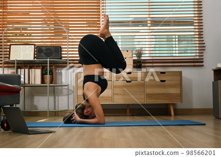 Strong woman practicing yoga, doing headstand pose on floor in living room. Healthy lifestyle, working out concept 98566201