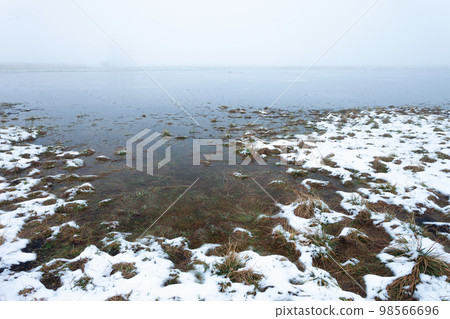 Water and snow on a flooded meadow in the foggy day Water and snow on a flooded meadow in the foggy day 98566696