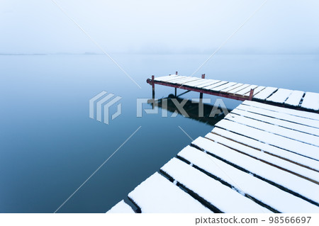 A snow-covered pier with a calm lake on a foggy day A snow-covered pier with a calm lake on a foggy day 98566697
