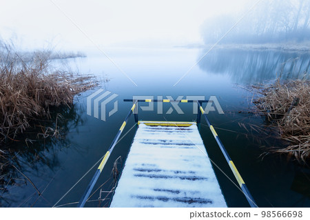 A pier with a handrail for disabled people on the shore of a lake on a foggy day A pier with a handrail for disabled people on the shore of a lake on a foggy day 98566698