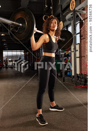 Athletic african american woman getting ready to do barbell squat in crossfit gym, hard workout. Athletic african american woman getting ready to do barbell squat in crossfit gym, hard workout. 98566736
