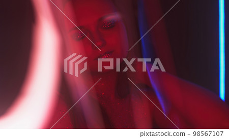 Color glow girl. Nightclub look. Disco fashion. Blur red neon light woman with shimmering face skin glitter artistic makeup metallic eyeshadow lips on dark free space. Color glow girl. Nightclub look. Disco fashion. Blur red neon light woman with shimmering face skin glitter artistic makeup metallic eyeshadow lips on dark free space. 98567107