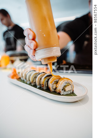Vertical view of the hands of unknown chief decorating tasty rolls with Japanese mayonnaise sauce 98567554
