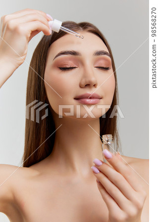 Organic products. Beautiful young girl applying face serum, taking care after skin over grey studio background. Concept of skincare and natural beauty 98568270