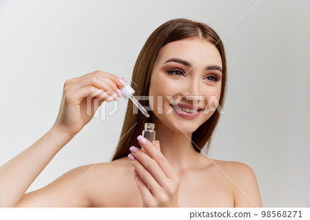 Portrait of young beautiful girl with healthy skin posing with face serum, toner over grey studio background. Concept of skincare and natural beauty 98568271