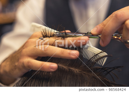 Close up of hairdressers hands cutting hair Close up of hairdressers hands cutting hair 98568424