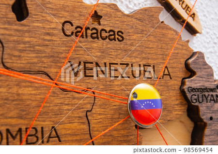 Venezuela flag on the pushpin with red thread showed the paths of movement or areas of influence in the global economy on the wooden map. Planning of traveling or logistic concept. Network connection Venezuela flag on the pushpin with red thread showed the paths of movement or areas of influence in the global economy on the wooden map. Planning of traveling or logistic concept. Network connection 98569454