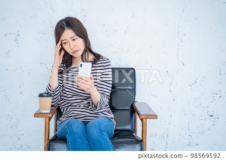 一位女士在客廳的椅子上拿著智能手機遇到麻煩 一位女士在客廳的椅子上拿著智能手機遇到麻煩 98569592