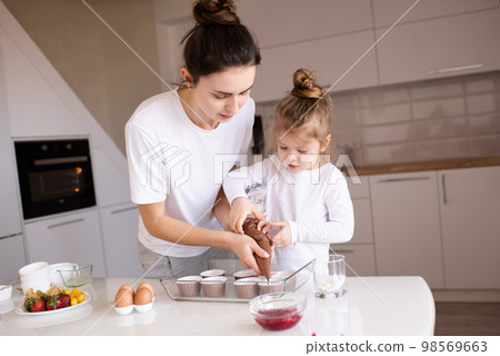 Young mother cook cupcakes with little child daughter 2-3 year old at home kitchen close up. Childhood. Motherhood. 98569663