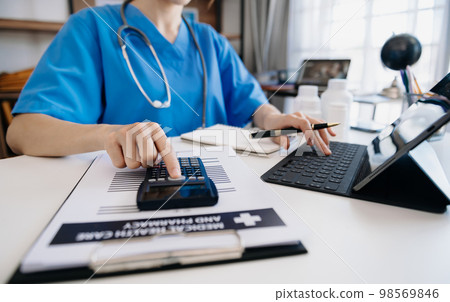 Healthcare costs and fees concept.Hand of smart doctor used a calculator and smartphone, tablet for medical costs at hospital in morning light 98569846