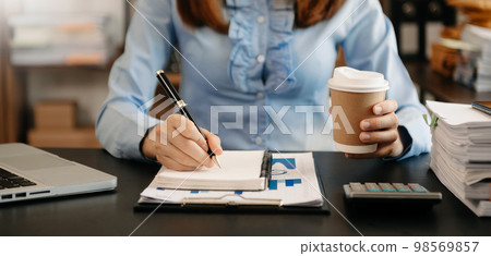 businesswoman hand writing on the notepad with new modern computer strategy diagram and holding coffee cup as concept morning light businesswoman hand writing on the notepad with new modern computer strategy diagram and holding coffee cup as concept morning light 98569857