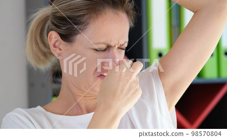 Worried woman with unhappy face checking smell of her armpit in office. 98570804