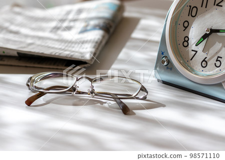 Glasses, a clock and a newspaper on the desk by the window Glasses, a clock and a newspaper on the desk by the window 98571110