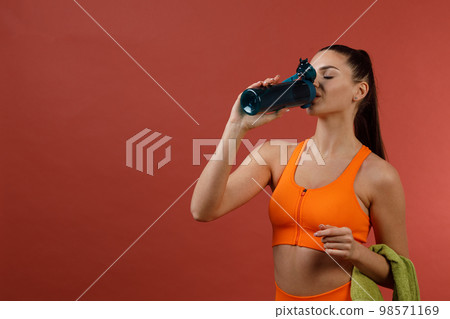 Young positive woman in orange fitness sport outfit cloth with bottle of water and towel after training 98571169