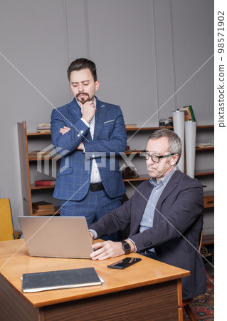 Businessman in dark blue suit with his partner are standing by laptop and working 98571902