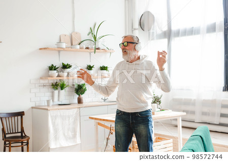 Happy senior man dancing while listening to music with headphones - active old people and enjoyment dance mood 98572744