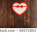 Gift box in the shape of a heart with a bow on a wooden textured background, top view 98572803