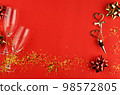 Still life with two empty glasses, a cork and a corkscrew with heart-shaped handles, golden confetti and bows on a red background 98572805