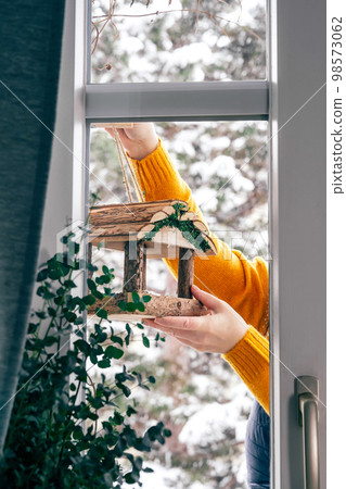 Woman hanging a bird feeder on balcony in winter. Urban birds life. Animal protection 98573062