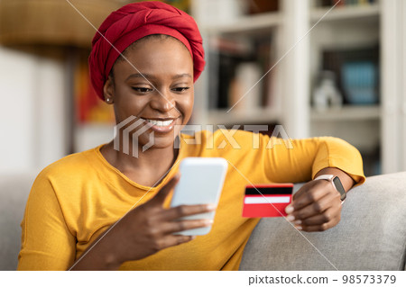Cheerful african american woman using credit card and phone, closeup Cheerful african american woman using credit card and phone, closeup 98573379